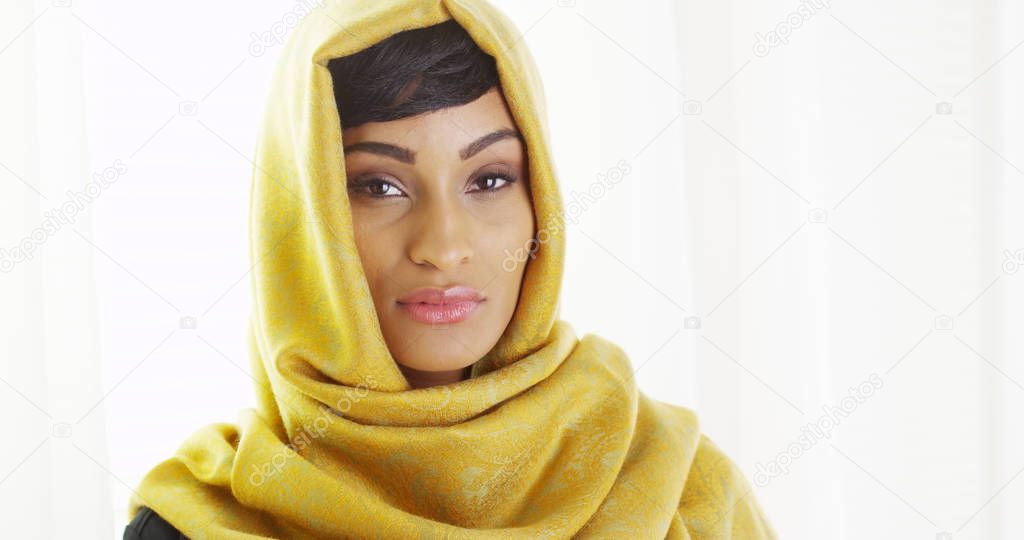 African woman wearing golden head scarf by window