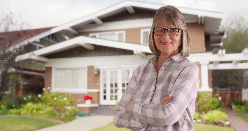 Happy senior woman smiling with arms crossed standing in front of her house