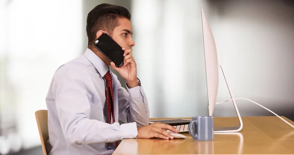 携帯電話で話しながらコンピューターで作業するヒスパニック ビジネス男性 — ストック写真