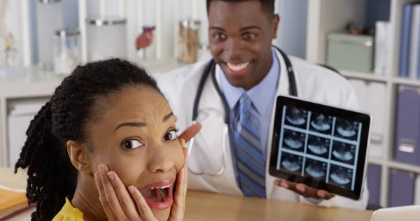 Black physician using tablet to show ultrasound to patient at desk