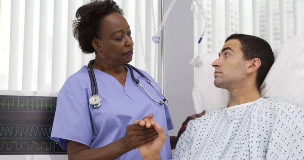 Senior black nurse comforting young hispanic patient on hospital bed