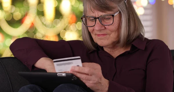 Tight shot of happy old lady on couch Christmas shopping online using pad device