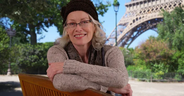 Happy smiling older woman tourist sitting on Park bench by Eiffel tower in Paris