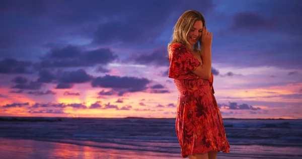 Middle aged Caucasian woman in sundress dancing on beach at sunset