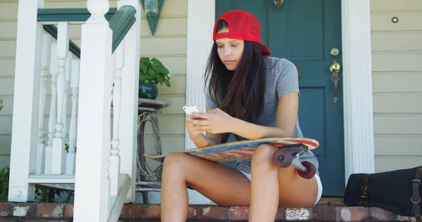 Mixed race woman sitting on porch with skateboard texting