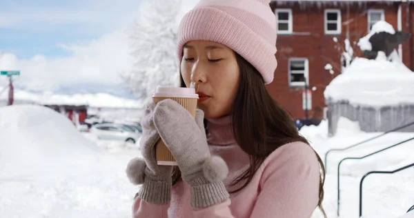 Close up of Asian millennial holding cup on snowy street