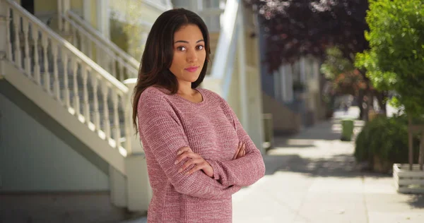 Young Latina female in pink sweater smiling at camera on quiet suburban street