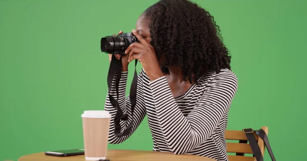 黑色女摄影师在绿色屏幕上的咖啡馆用相机拍照 — 图库照片