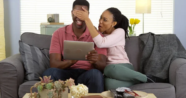 年轻的黑人妇女覆盖男友的眼睛 因为他浏览网页上的平板电脑 — 图库照片
