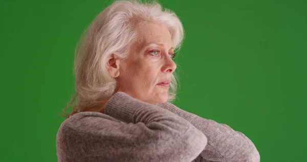 Portrait of woman with neck pain rubbing neck looking off screen on green