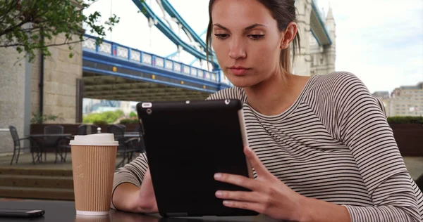 Millennial woman sitting at cafe table with tablet in London by Tower Bridge