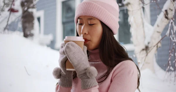 Close up of Asian millennial holding cup in front of snowy house