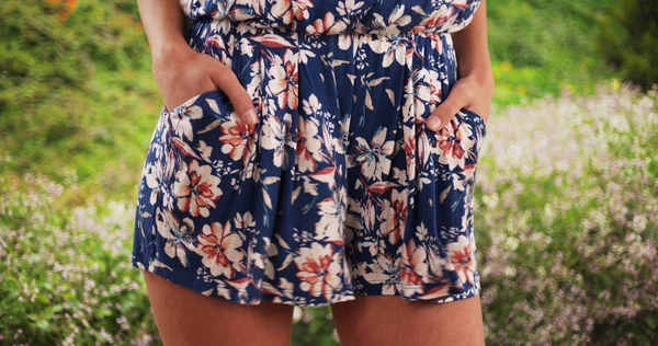 Close-up of stylish womans hands in romper pockets outside near some flowers