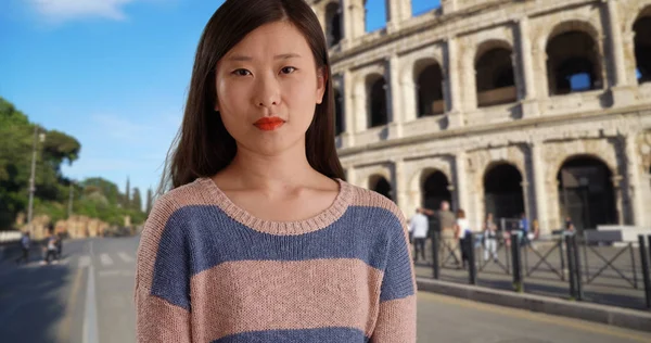 Close-up of confident millennial woman in a sweater in front Colosseum in Rome