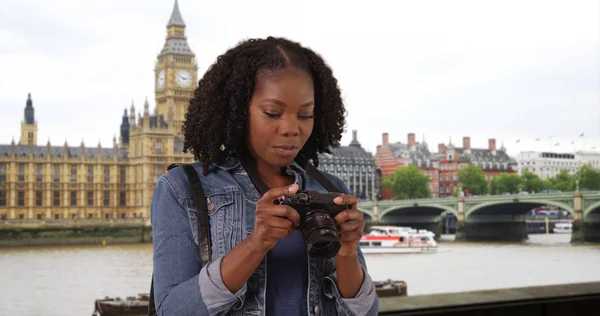 Portrait of black woman standing by River Thames in London taking pictures