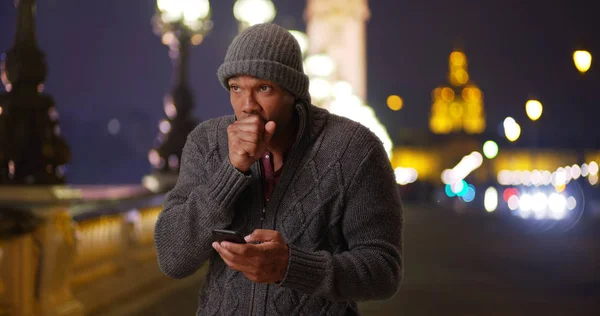 Cold black male on Pont Alexandre III in Paris texting friend on cold night