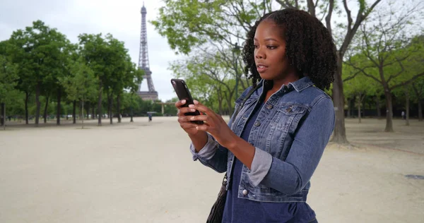 Pretty black woman on vacation in Paris using map app on cell phone