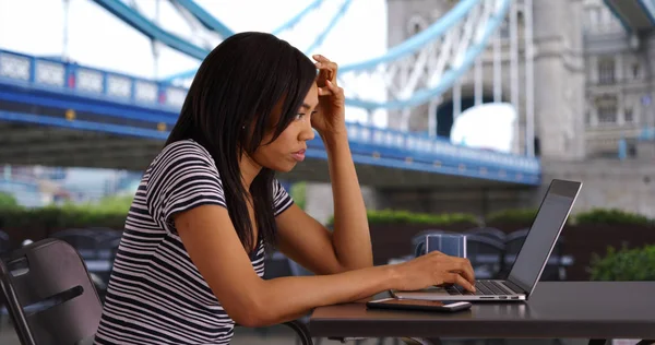 Black woman on vacation in London answering work emails on laptop