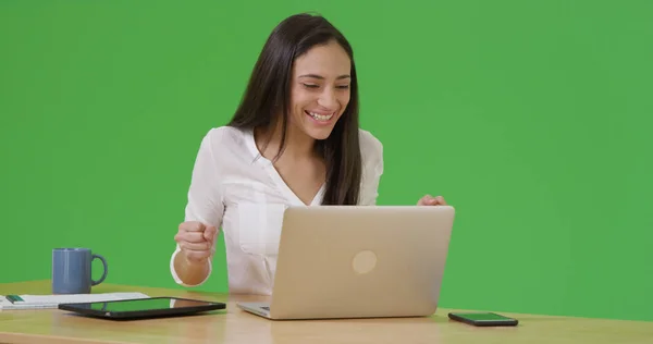A Latina woman celebrates as she uses her laptop on green screen