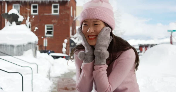 Close up of cute woman sitting in pose with mittens and beanie on snowy street