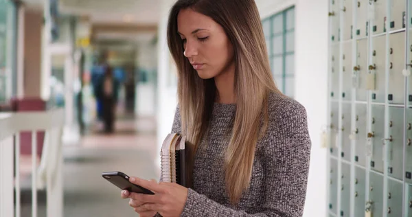 Millennial Mulher Estudante Mensagens Texto Telefone Enquanto Segurando Livros Corredor — Fotografia de Stock