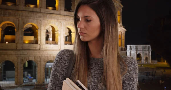 Serious millennial woman student holding books looking offscreen in Rome
