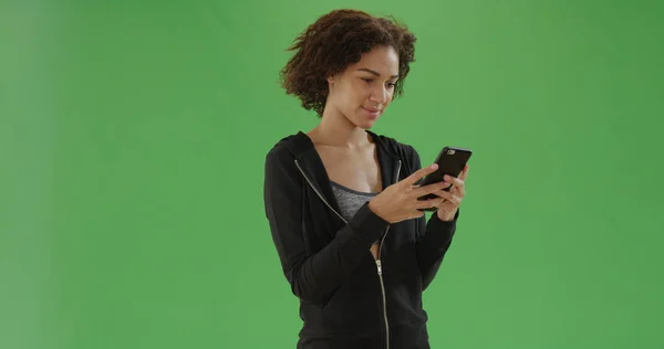 Young african American girl in workout attire uses smart phone on green screen