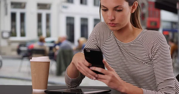 カフェ テーブルのテキスト メッセージで市でテーブルに座って携帯電話で座っている若い女性 — ストック写真