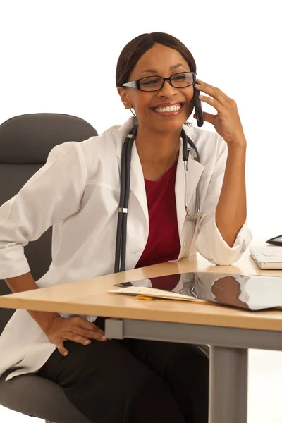 笑みを浮かべながら電話で話している机に座って幸せ千年黒い医者 — ストック写真