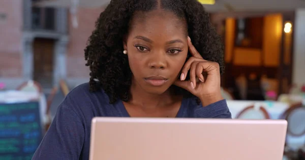 Unhappy black woman has to work on vacation uses laptop at cafe in Rome