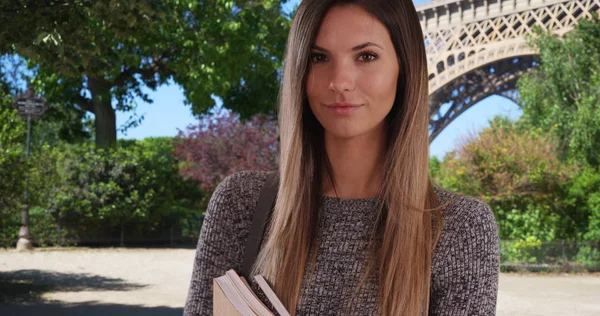 Confident female exchange student holding books posing near Eiffel Tower