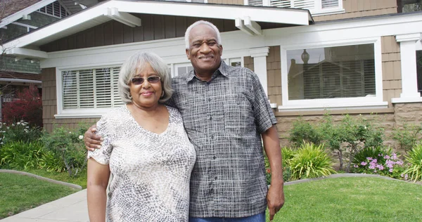 Happy elderly black couple standing on front yard