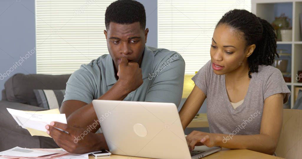 Worried young African American couple looking through bills online