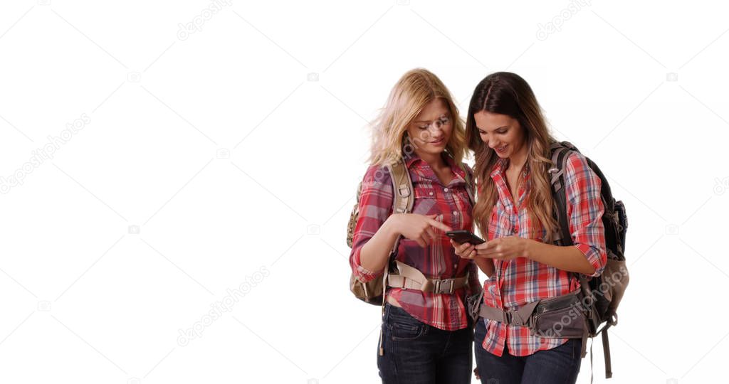 Two women backpackers using cell phone on white background with copy space