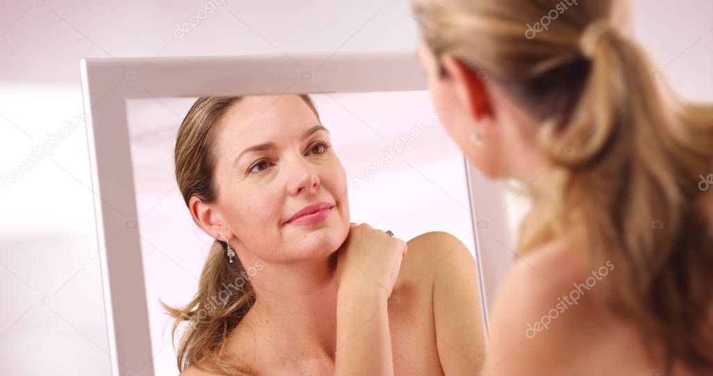 Middle aged Caucasian woman looking at reflection in mirror in the morning