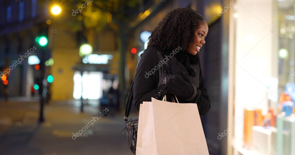 Lovely black woman stops to look at store window in shopping area at night