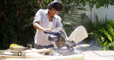 Black woman doing home improvement cutting wood with a table saw clipart