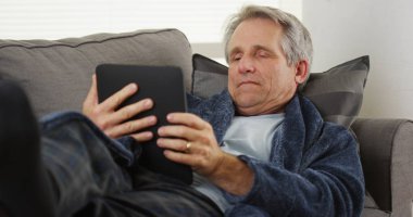 Bir tablet okuma kanepede yatan yorgun orta yaşlı adam