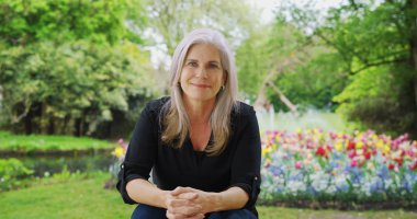 Yemyeşil bahçede sıcak oturan eski mutlu beyaz kadın kameraya benziyor 