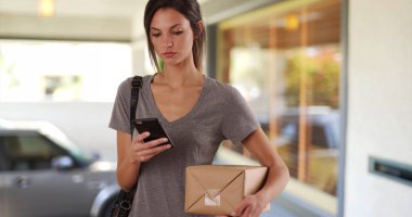 Evinin önünde posta paket ayakta tutarak cep telefonu kullanan kadın