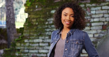 Taş duvar tarafından kameraya bakarak neşeli ifade ile Afrikalı-Amerikalı kadın