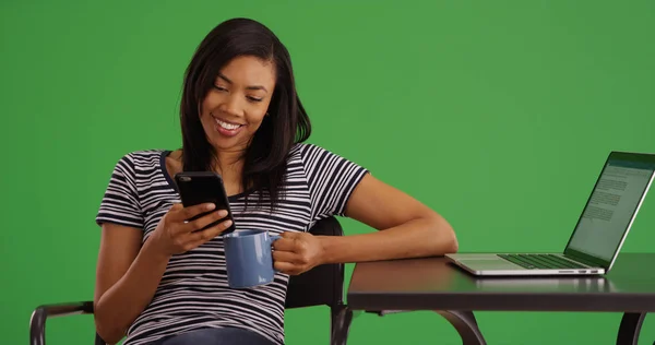 Smiling black woman with coffee using mobile device at cafe on green screen