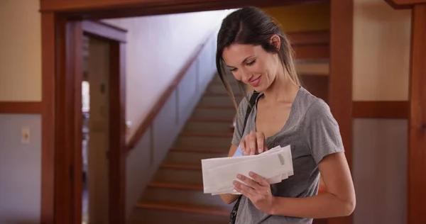 White millennial female checking stack of letters standing inside her house