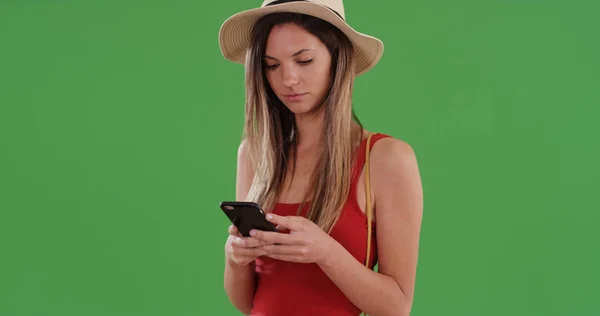 Millennial woman in red top and fedora using cellphone app on greenscreen