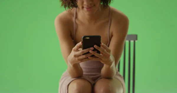 緑色の画面上の木の椅子に座っている彼女の携帯電話を使用して若い黒人女性 — ストック写真