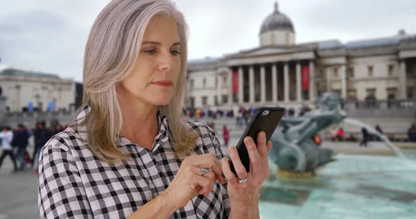 Mature Caucasian female checks phone at Trafalgar Square in London