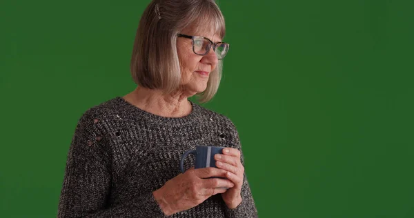 白人高齢者女性探して緑色の画面で物思いに沈んだコーヒーのマグカップを保持 — ストック写真