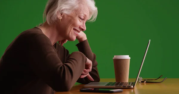 快乐的老太婆在笔记本电脑上滚动的侧面轮廓与绿色屏幕上的咖啡 — 图库照片