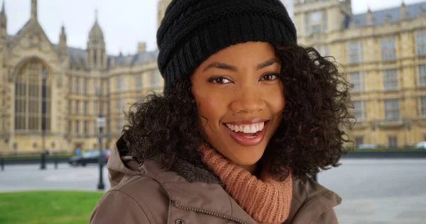 Happy black woman tourist smiling in front of Westminster Palace during winter