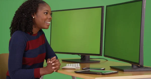 Black businesswoman using dual monitor desktop with green screens on display